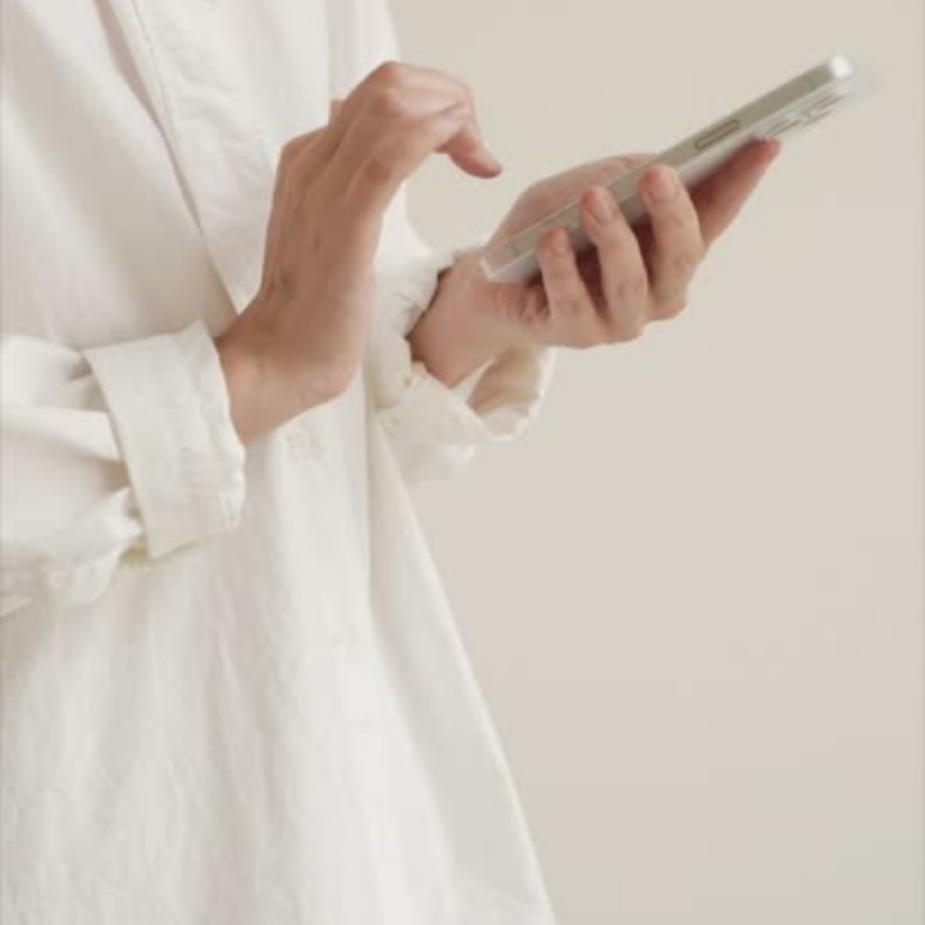 A person in a white shirt using a smartphone, focusing on their hands holding the device.