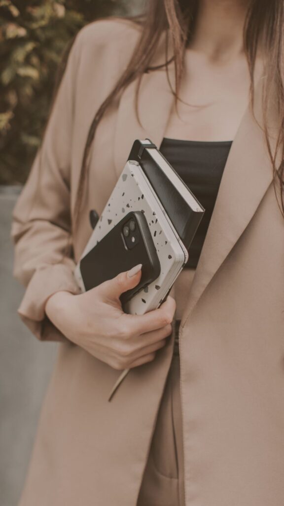 A woman in a beige blazer holding a stylish polka dot clutch with a smartphone peeking out.