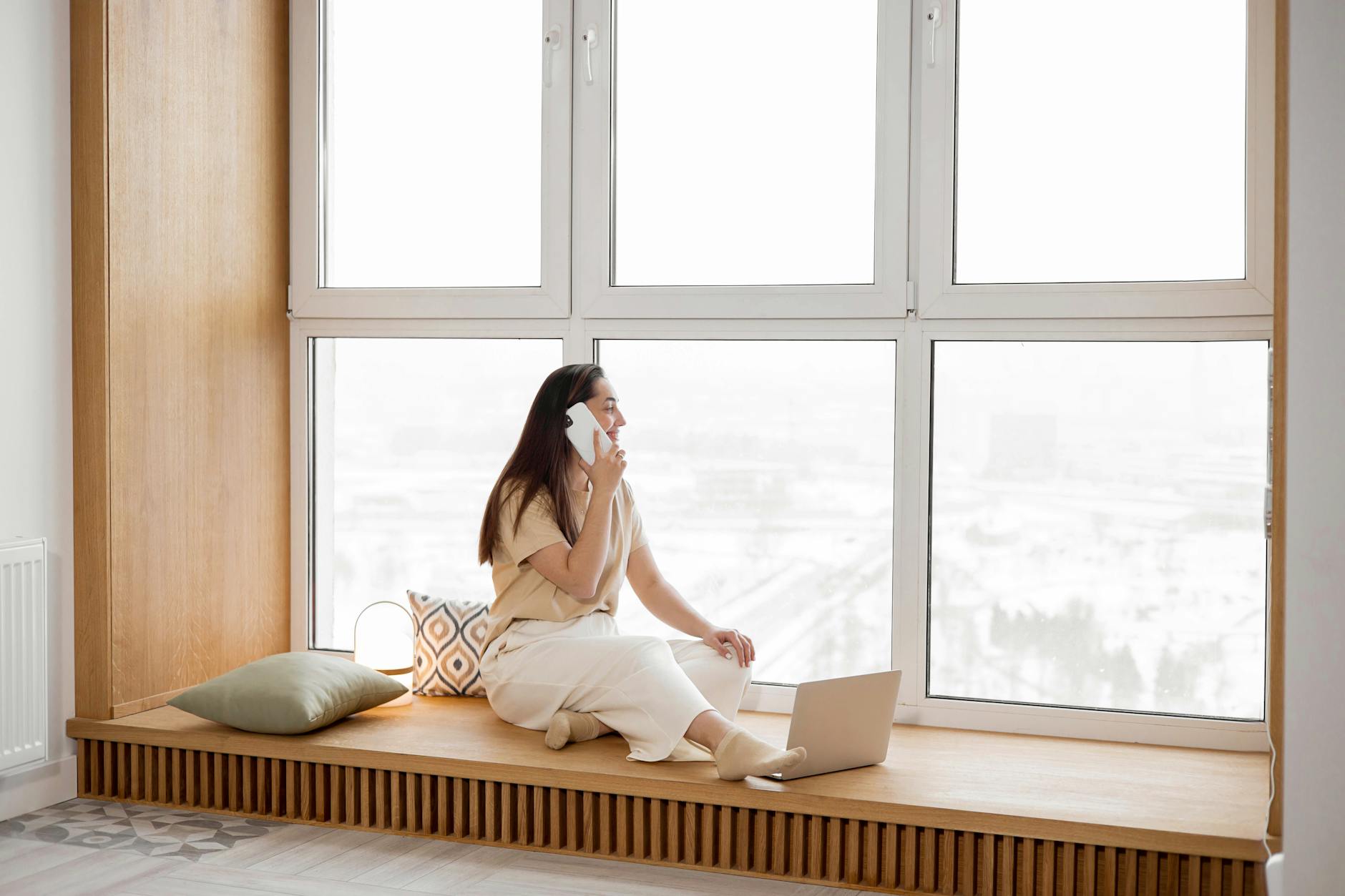 a woman talking on the phone while sitting beside the window