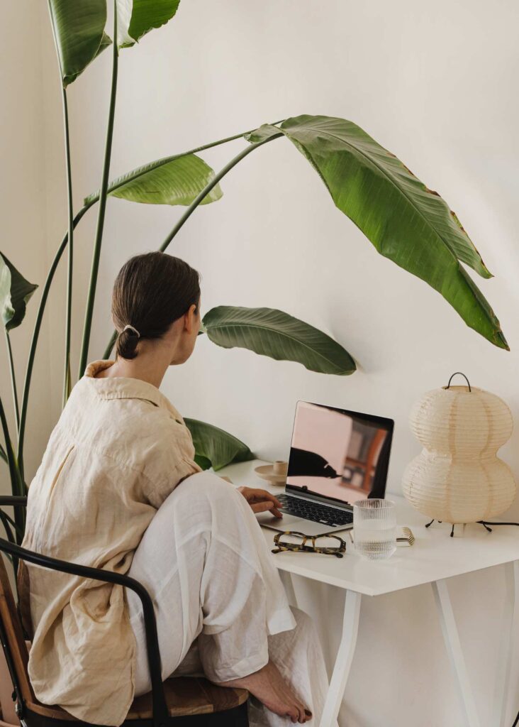 Modern, minimalist workspace featuring a cozy natural aesthetic with a laptop, greenery, and soft lighting. Perfect for showcasing intentional branding design and creative services that resonate with thoughtful, aligned clients.